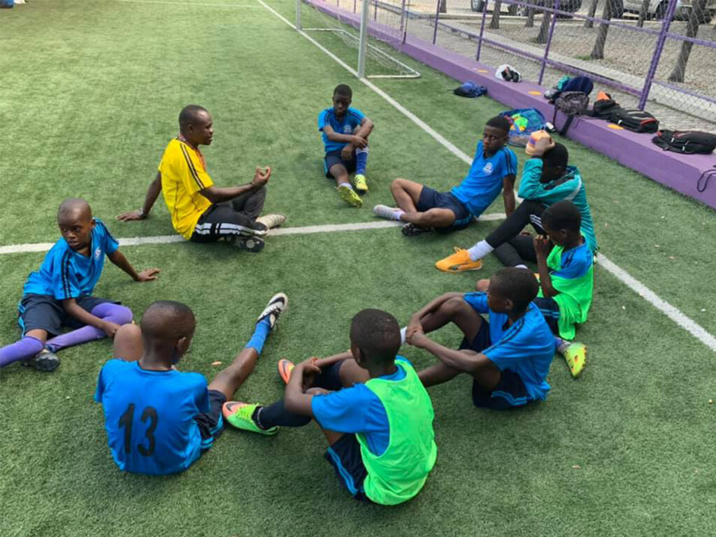 Entra&icirc;neur enseignant &agrave; un groupe de footballeurs assis &agrave; Ambassadors Football Haiti