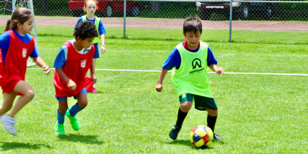 kids kicking a soccer ball outside wearing practice jerseys