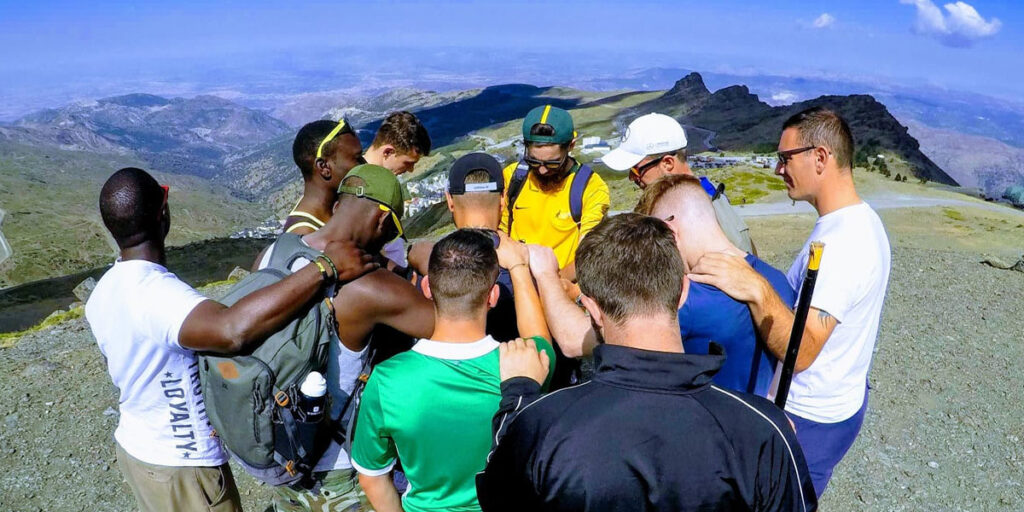 team praying together on top of a mountain in spain
